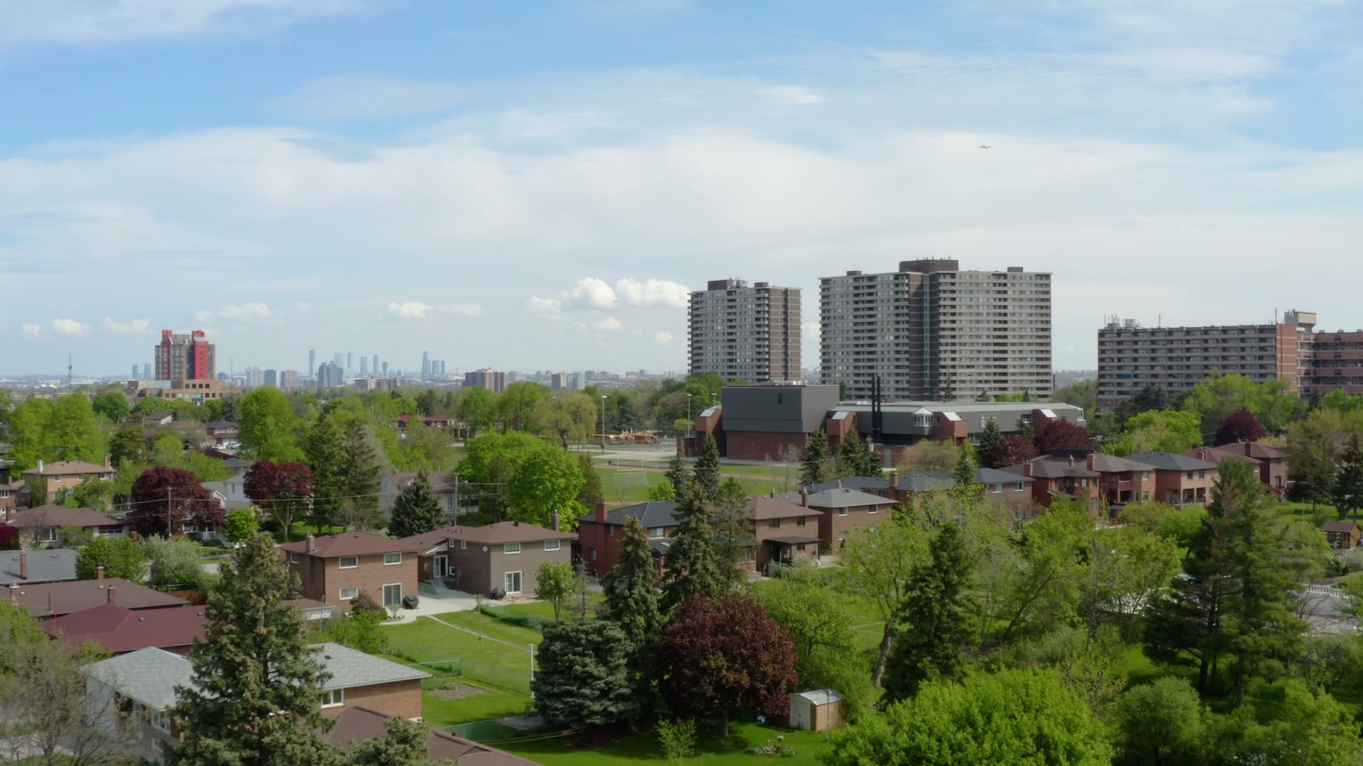 Aerial view over a North York residential neighbourhood on the Bathurst corridor, brick homes and mature trees with apartment towers and the Toronto skyline beyond.